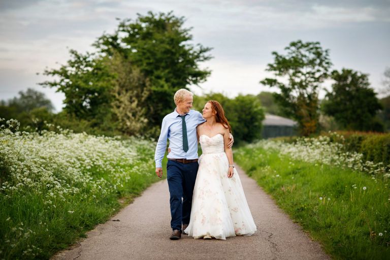 Couple walk back to their guests arm in arm surrounded by cow parsley after their humanist outside wedding