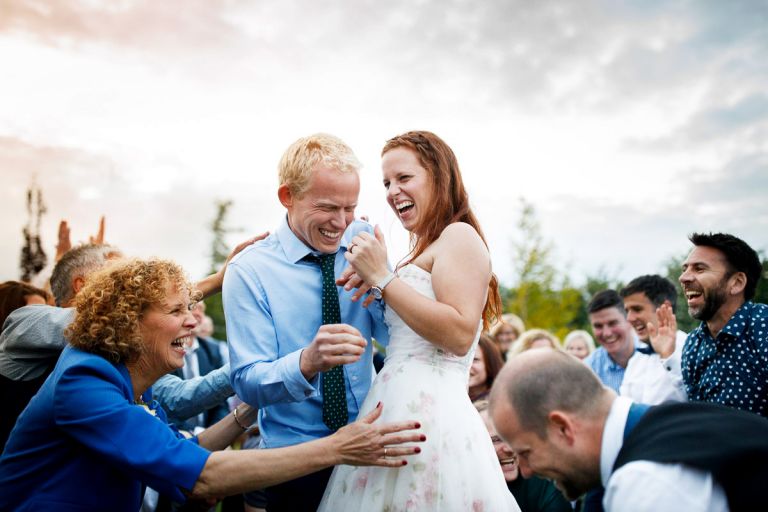 Couple laugh as all their guests try to touch them during ceilidh dance during their humanist outside wedding