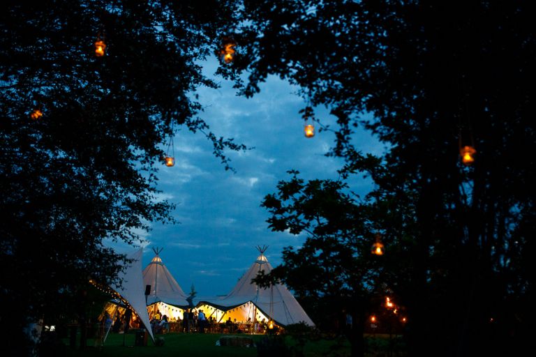 Tipi all lit up at night as seen through trees with candles hung in them, tipi at humanist outside wedding