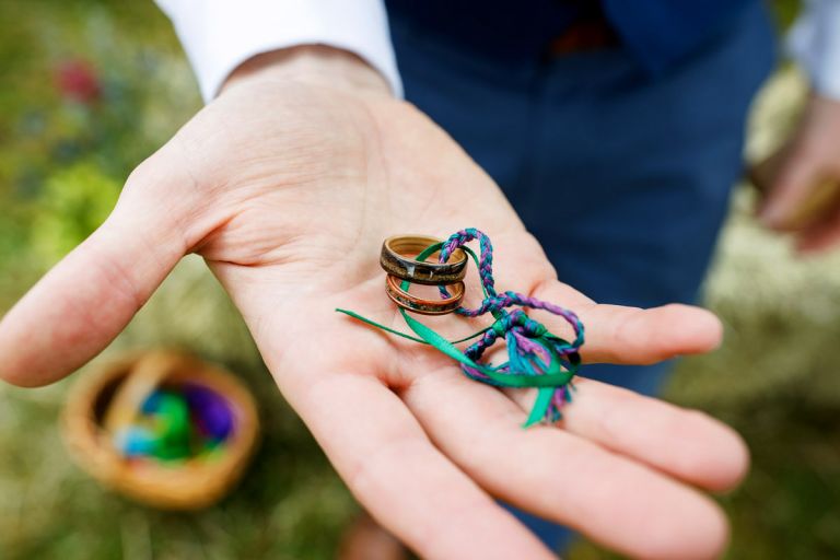 Eco Wood Rings wedding rings, two for the bride and groom, held out in a hand, they are tied together with colourful plaited ribbon. 