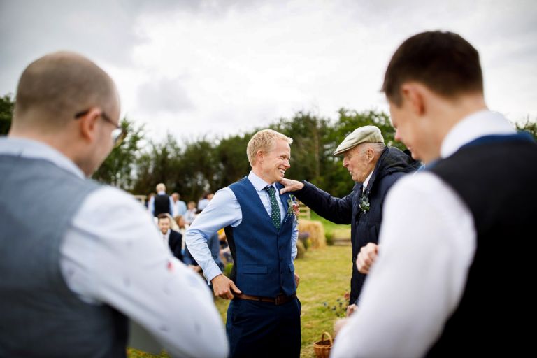 Groom's grandfather rests his hand on the groom's shoulder as he gives him advice before the outside ceremony