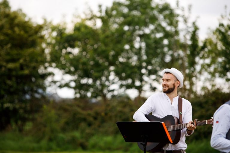 A man plays guitar and sings for guests arriving at the outside wedding ceremony