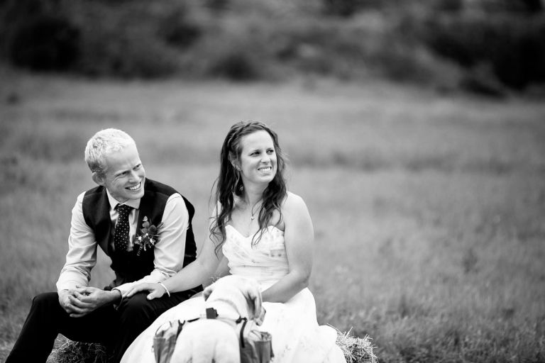 Black and white photo of couple listening to their ceremony, bride puts her hand on the grooms leg as nice things are said about him.