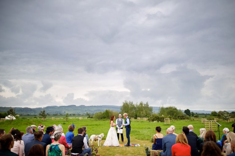 Couple read vows during their outdoor wedding ceremony, hills in the distance and grey skies overhead. 