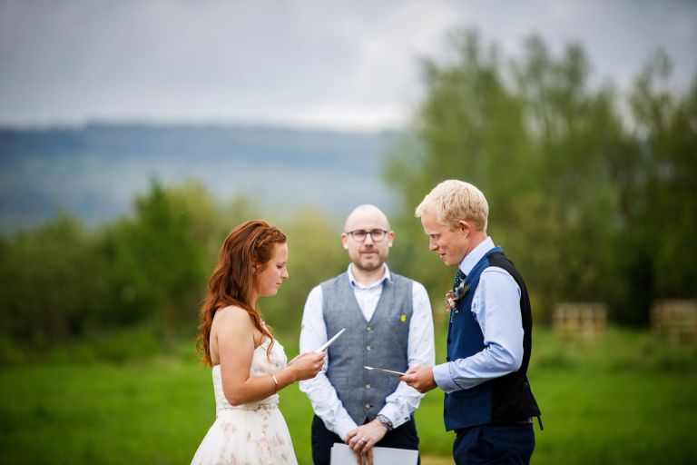 Close up of couple reading their vows together during their outside wedding, surrounded by trees and greenery. 