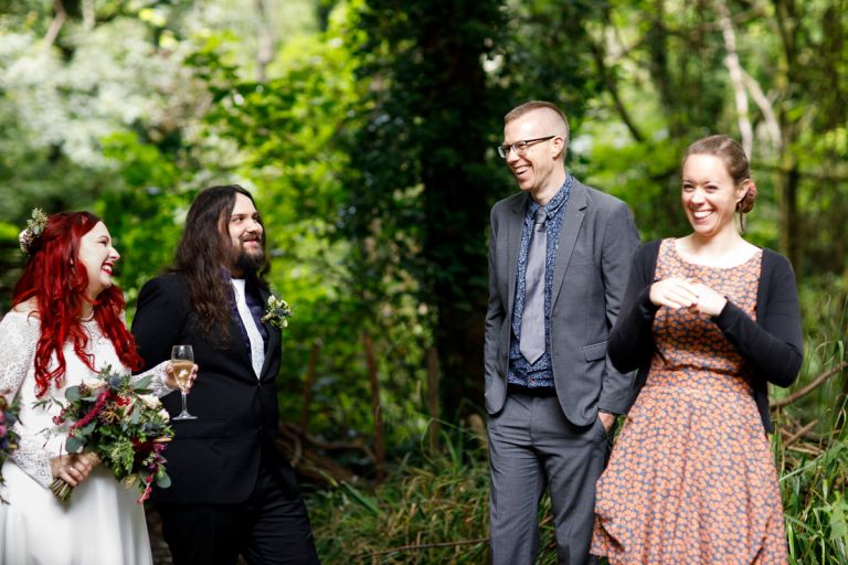 Guests laugh with couple at wedding in a forest