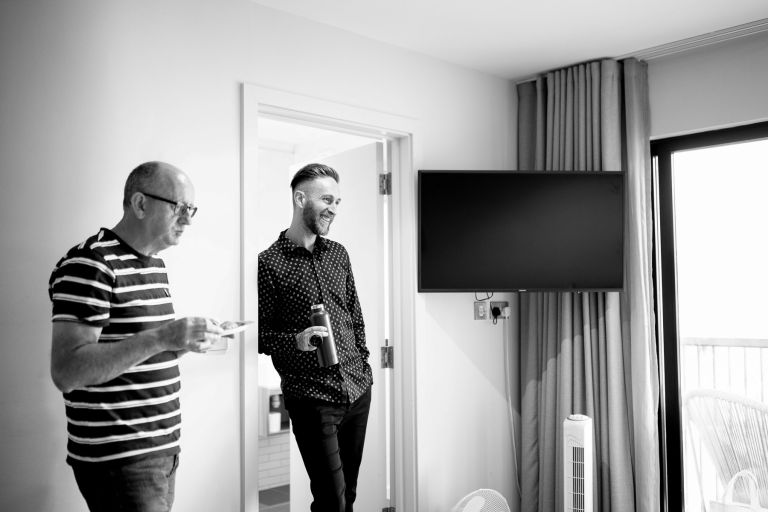 Groom looks on at his bride getting ready while smiling