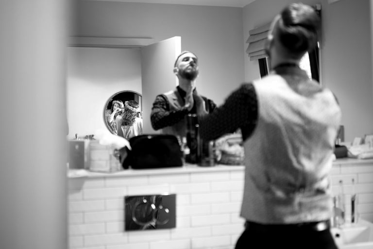 Groom is blurred out as he gets ready, bride's reflection is seen getting ready in the background