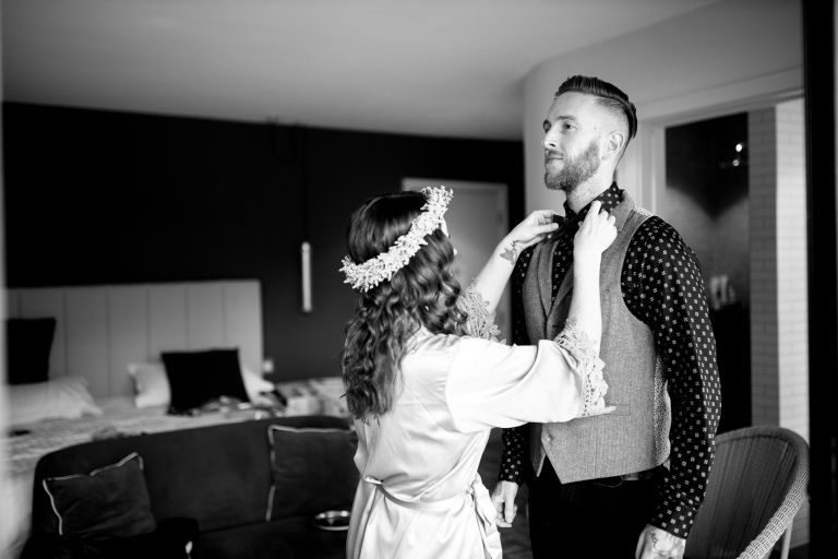 Bride helps her groom get ready by doing up his bow tie.