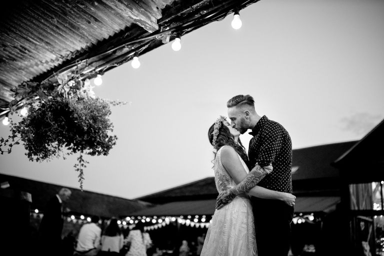 Couple kiss under festoon lights at barn in Gloucester