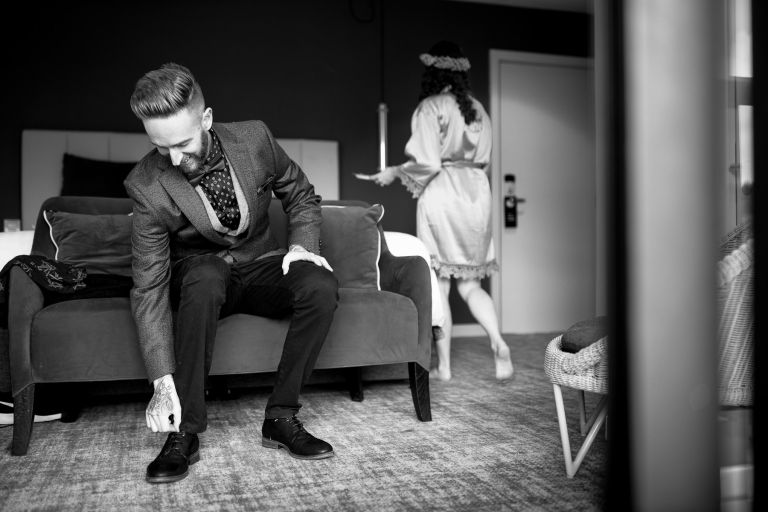 Groom puts on shows while bride is in the background as they both get ready for their wedding at The Over Barn