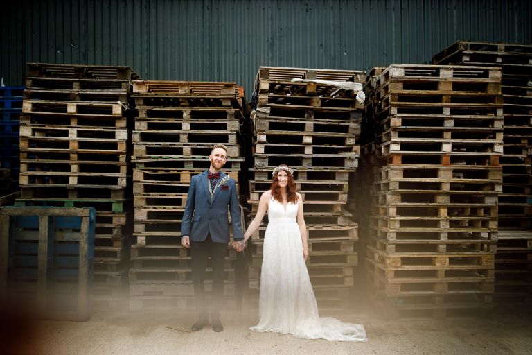 The Over Barn creative wedding photo in front of a stack of pallets. 