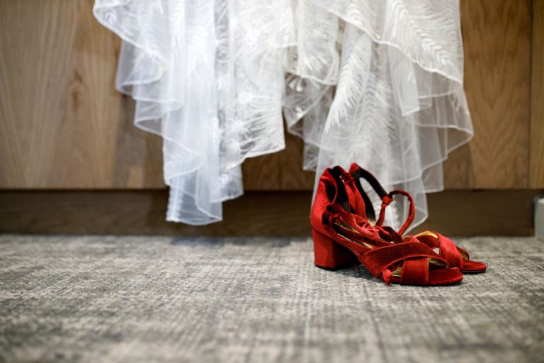 Bride's red shoes in front of the bottom of her dress hanging up