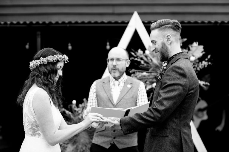 Bride places ring on grooms finger at Outside wedding ceremony at The Over Barn Gloucester