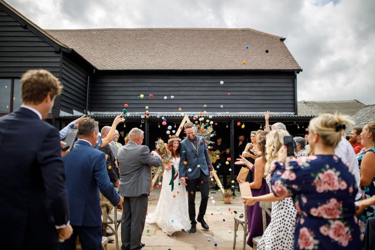 Couple exit outdoor ceremony to colourful pom pom confetti