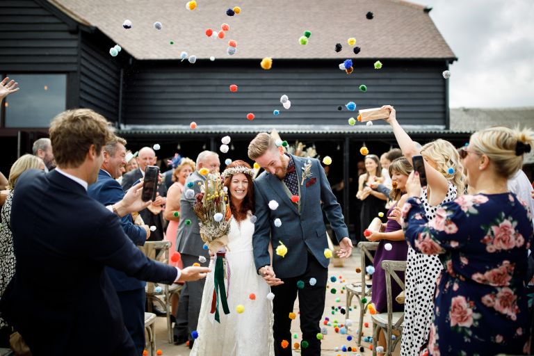 Couple walk up the aisle to pompom confetti at The Over Barn in Gloucester