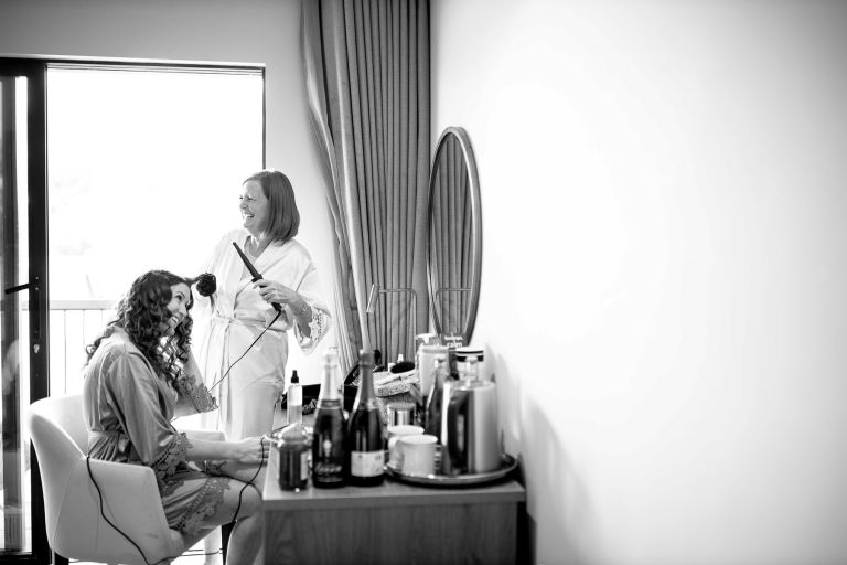 Bride's mother does the bride's hair while they both laugh