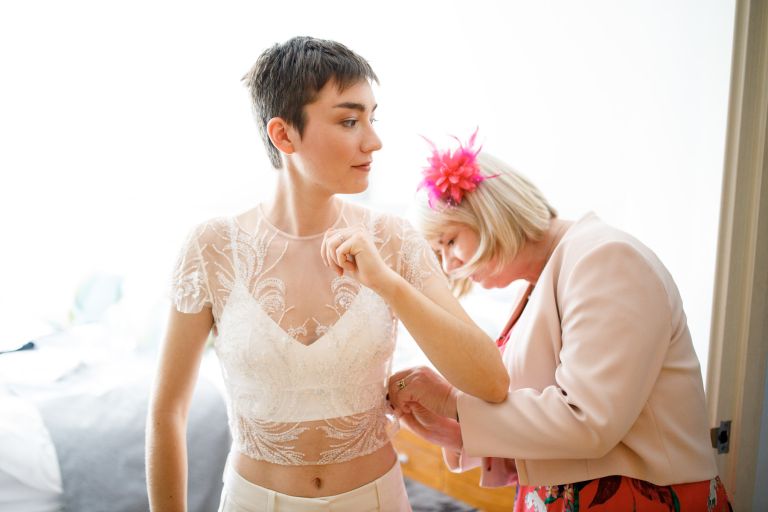 Bride with short hair has wedding clothes put on by mother, at Bristol same sex wedding