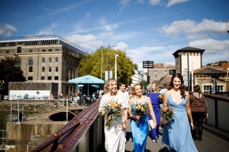 Bride walks with her best people over Prince Street Bridge with Alnofini in the background