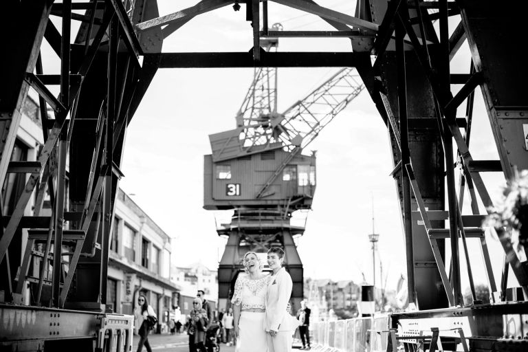 Brides laugh during portraits under crane in Bristol 