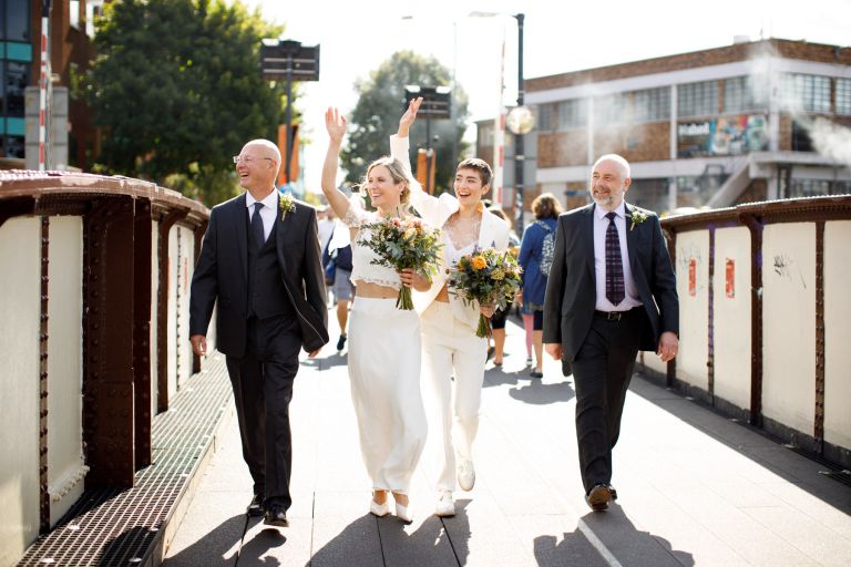 Brides wave from Prince Street Bridge with Dads on their way to same sex wedding at the mud dock