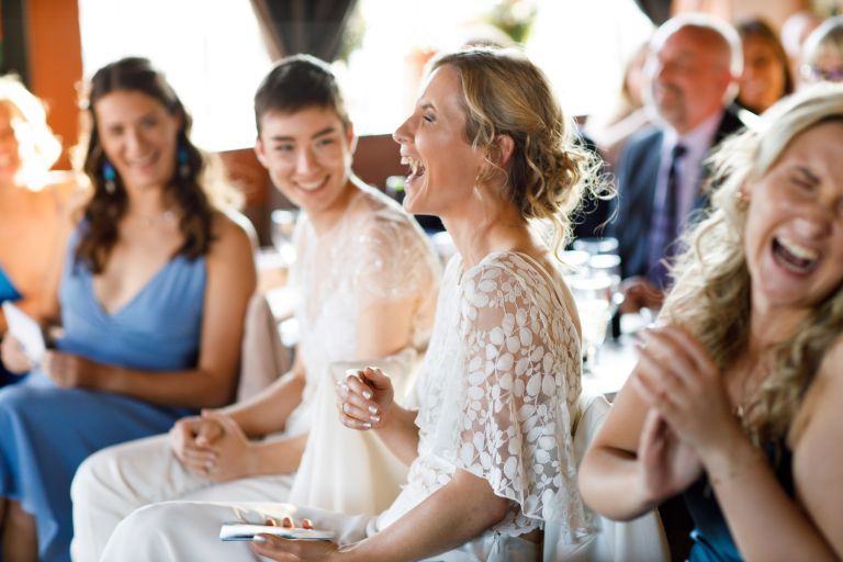 bride and guests laugh hard at wedding speech at the mud dock